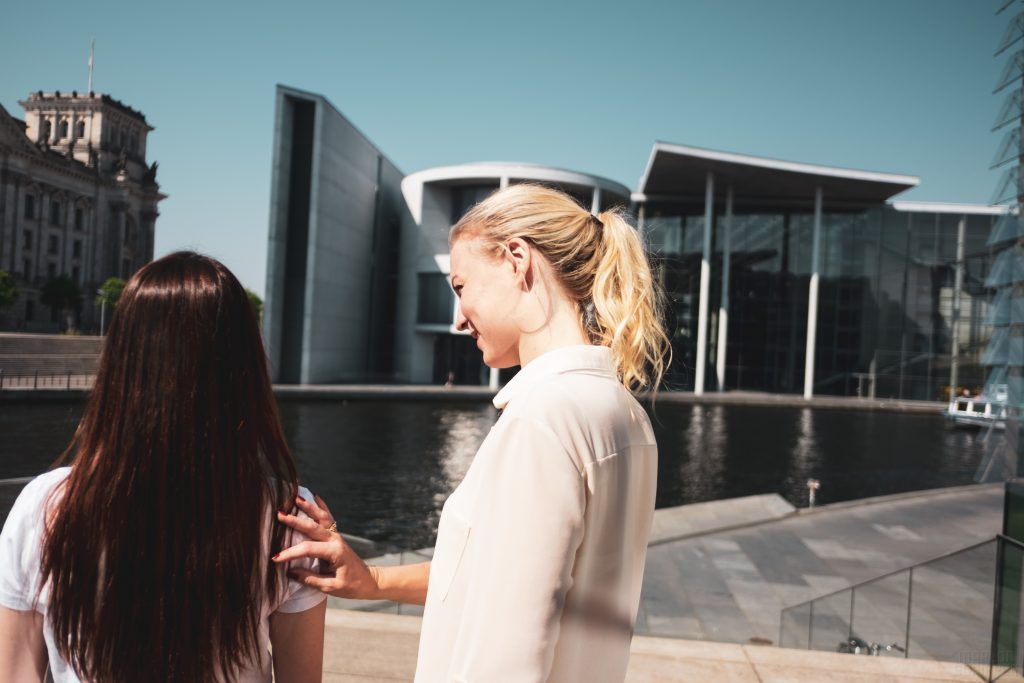 Zwei junge Frauen mit Blick Richtung Zukunft. Die eine hält ihre Hand unterstützend auf die Schulter der anderen.